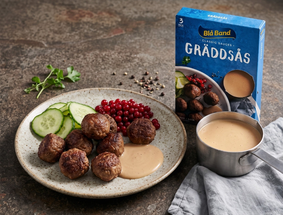 Blå Band Gräddsås Swedish cream sauce served over Swedish meatballs with lingonberries and cucumber on a plate, sauce box in background
