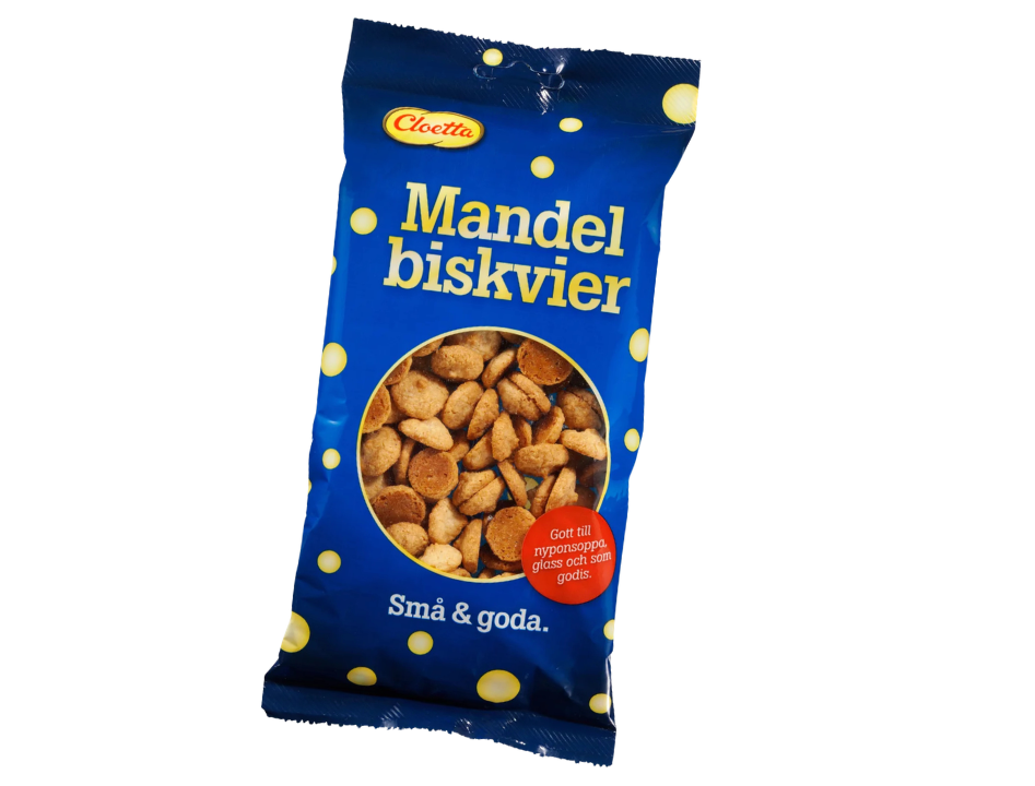 Cloetta Mandelbiskvier 150g – dark blue bag with yellow polka dots, Mandelbiskvier in bold yellow lettering, Cloetta oval logo, round window showing small golden almond biscuits, Små & goda, Gott till nyponsoppa glass och som godis, 150g
