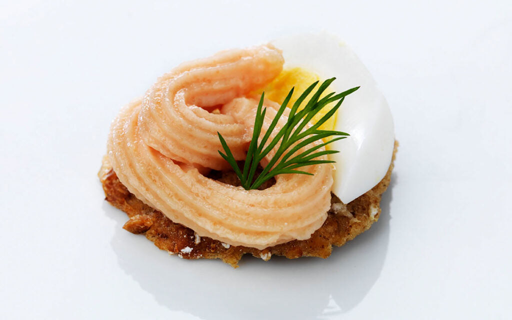 Kalles Kaviar Original piped in a swirl on a piece of Swedish crispbread with a soft-boiled egg half and fresh dill, served on a white plate
